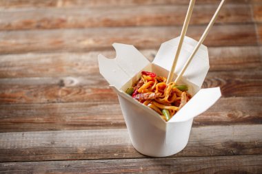 Domuz eti ve sebzeli erişte, ahşap masadaki paket kutusunda.