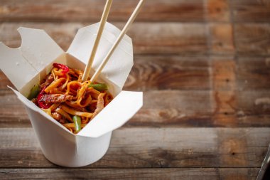 Domuz eti ve sebzeli erişte, ahşap masadaki paket kutusunda.