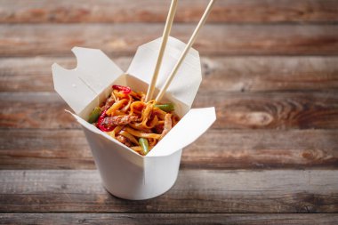 Domuz eti ve sebzeli erişte, ahşap masadaki paket kutusunda.