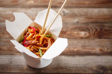 Domuz eti ve sebzeli erişte, ahşap masadaki paket kutusunda.