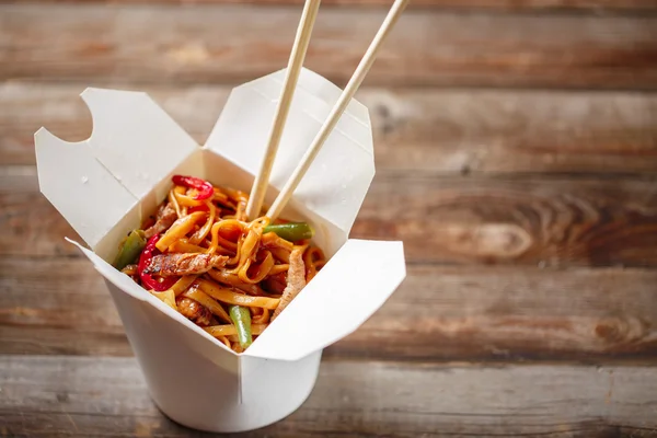 Noodles with pork and vegetables in take-out box on wooden table — Stock Photo, Image