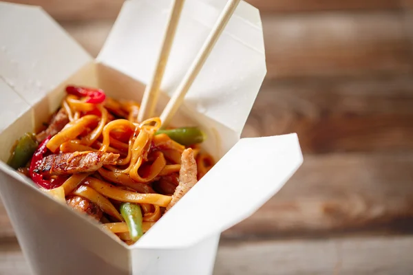 Fideos con cerdo y verduras en caja para llevar sobre mesa de madera —  Fotos de Stock