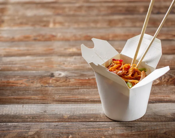 Fideos con cerdo y verduras en caja para llevar sobre mesa de madera —  Fotos de Stock