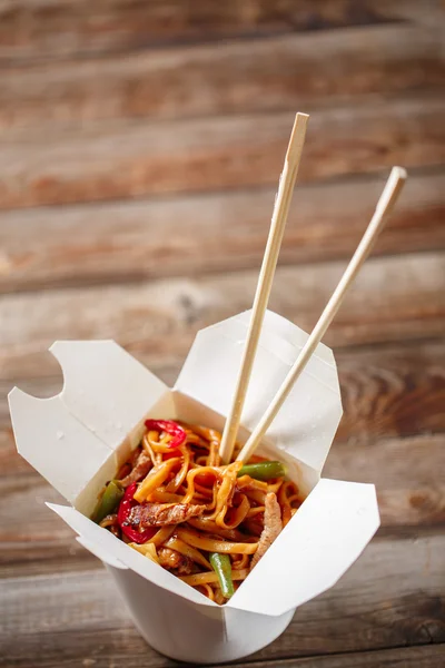 Fideos con cerdo y verduras en caja para llevar sobre mesa de madera —  Fotos de Stock