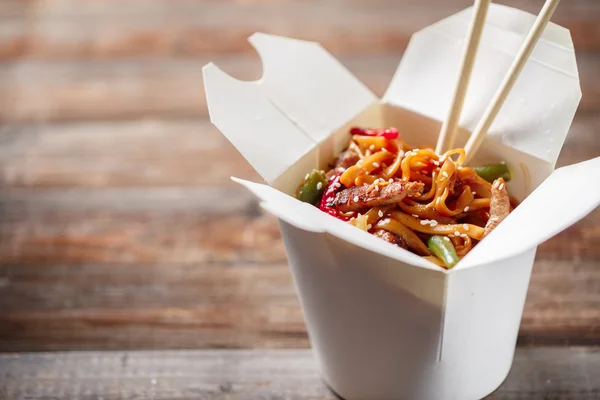 Fideos con cerdo y verduras en caja para llevar sobre mesa de madera —  Fotos de Stock