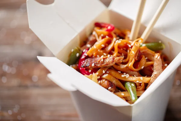 Fideos con cerdo y verduras en caja para llevar sobre mesa de madera —  Fotos de Stock