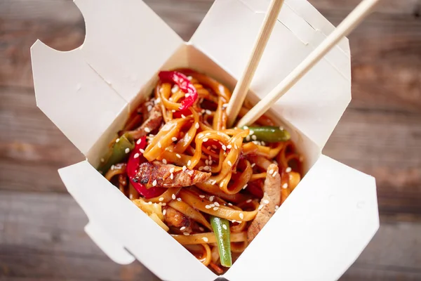 Nudlar med fläsk och grönsaker i take-out box på träbord — Stockfoto