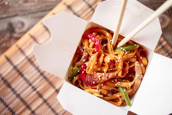 Fideos con cerdo y verduras en caja para llevar sobre mesa de madera —  Fotos de Stock