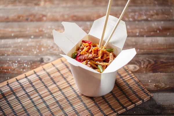 Noodles with pork and vegetables in take-out box on wooden table — Stock Photo, Image