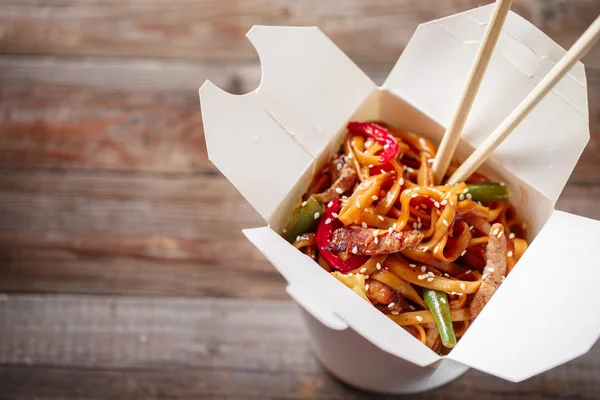 Noodles with pork and vegetables in take-out box on wooden table — Stock Photo, Image