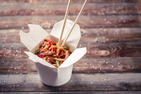 Fideos con cerdo y verduras en caja para llevar sobre mesa de madera —  Fotos de Stock