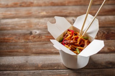 Domuz eti ve sebzeli erişte, ahşap masadaki paket kutusunda.