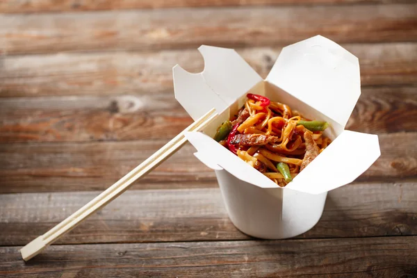 Fideos con cerdo y verduras en caja para llevar sobre mesa de madera —  Fotos de Stock