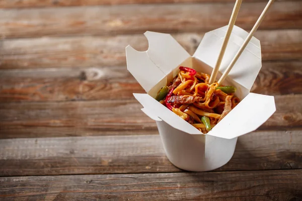 Fideos con cerdo y verduras en caja para llevar sobre mesa de madera —  Fotos de Stock