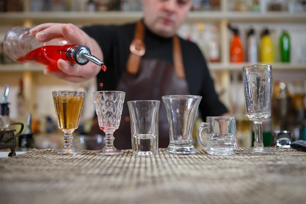 Barman nalewa różnych pić alkohol w małych szklankach na pasek — Zdjęcie stockowe