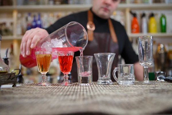 Barman nalévá různé alkoholického nápoje do malých sklenic na baru — Stock fotografie