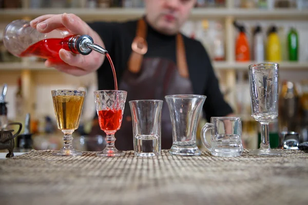 Cantinero vierte varios de bebida alcohólica en vasos pequeños en la barra — Foto de Stock