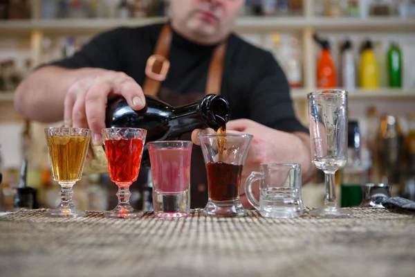 Barman nalewa różnych pić alkohol w małych szklankach na pasek — Zdjęcie stockowe