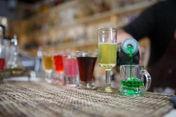 Barman nalévá různé alkoholického nápoje do malých sklenic na baru — Stock fotografie