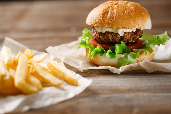 Homemade burger and french fries on a wooden plate — Stock Photo, Image