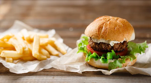 Homemade burger and french fries on a wooden plate — Stock Photo, Image