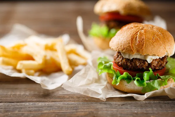 Hemgjord välsmakande hamburgare och pommes frites på träbord — Stockfoto