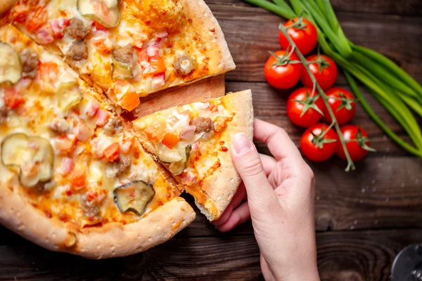 Hand picking tasty slice of pizza lying on wooden table