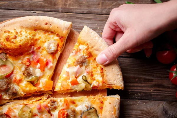 Hand picking tasty slice of pizza lying on wooden table — Stock Photo, Image