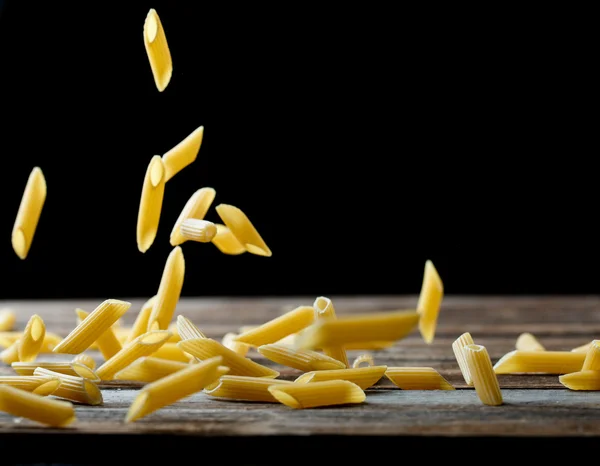 Falling penne pasta. Flying yellow raw macaroni over black background. — Stock Photo, Image