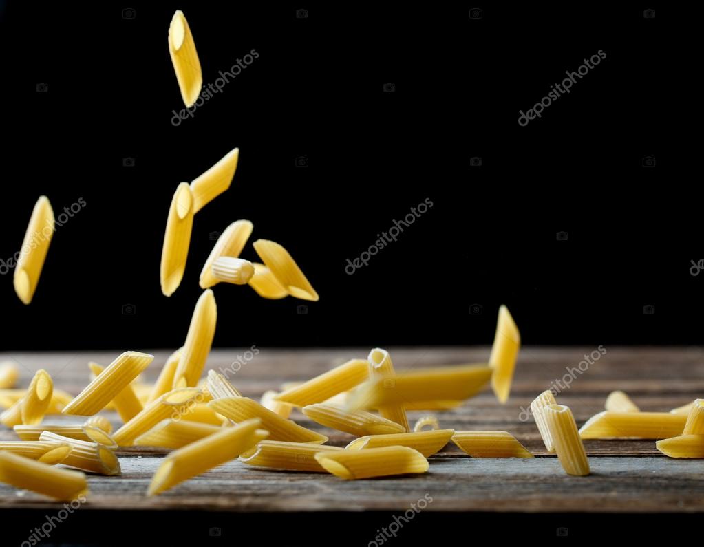 Falling penne pasta. Flying yellow raw macaroni over black background