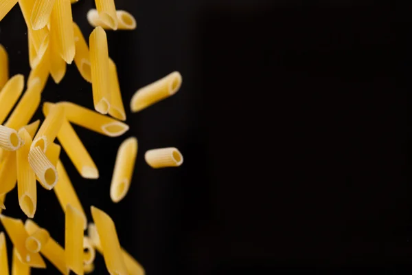 Falling penne pasta. Flying yellow raw macaroni over black background. — Stock Photo, Image