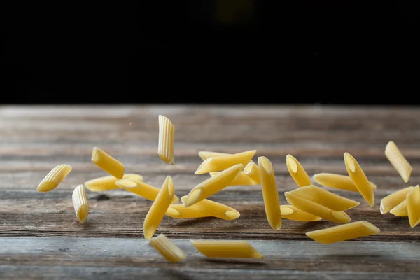 Falling penne pasta. Flying yellow raw macaroni over black background. — Stock Photo, Image