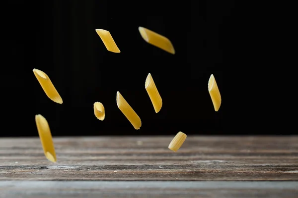 Fallende Penne-Pasta. Fliegende gelbe rohe Makkaroni über schwarzem Hintergrund. — Stockfoto