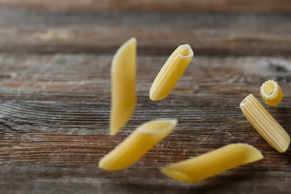 Fallende Penne-Pasta. Fliegende gelbe rohe Makkaroni über schwarzem Hintergrund. — Stockfoto