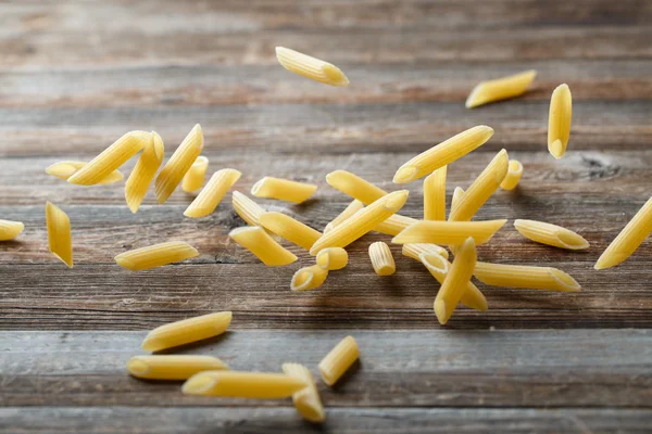 Falling penne pasta. Flying yellow raw macaroni over black background. — Stock Photo, Image