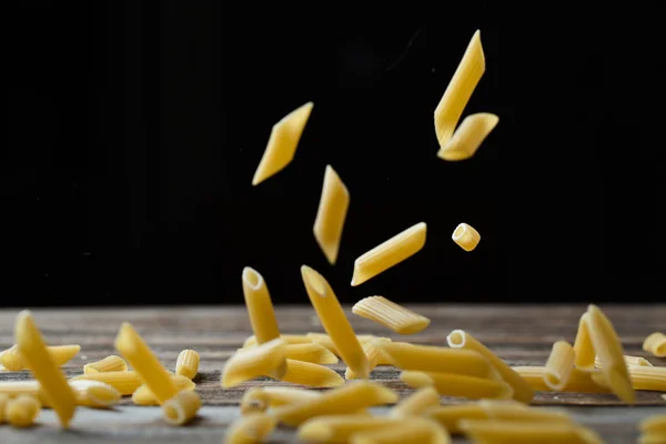 Falling penne pasta. Flying yellow raw macaroni over black background. — Stock Photo, Image