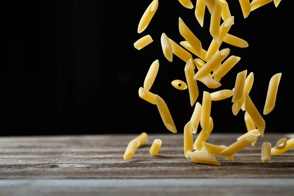 Fallende Penne-Pasta. Fliegende gelbe rohe Makkaroni über schwarzem Hintergrund. — Stockfoto