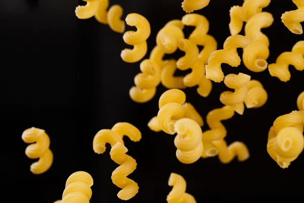 Falling cavatappi pasta. Flying yellow raw macaroni over black background. — Stock Photo, Image