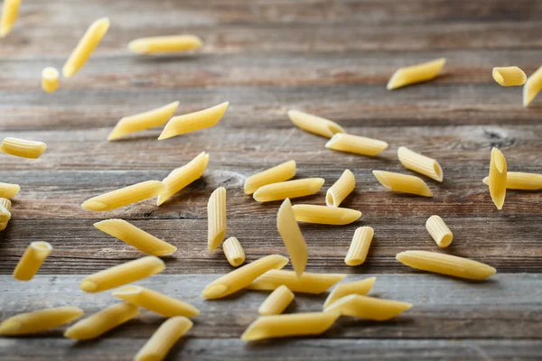 Falling penne pasta. Flying yellow raw macaroni over black background. — Stock Photo, Image