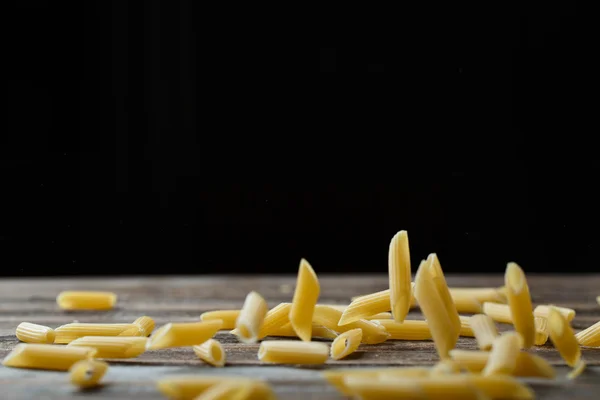 Caída de pasta de penne. Macarrones crudos amarillos voladores sobre fondo negro. — Foto de Stock