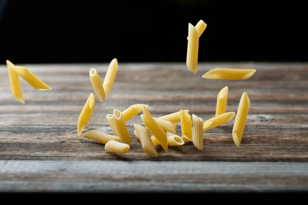 Massa de penne a cair. Voando macarrão cru amarelo sobre fundo preto. — Fotografia de Stock