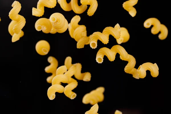 Falling cavatappi pasta. Flying yellow raw macaroni over black background. — Stock Photo, Image