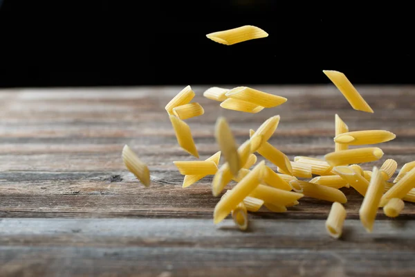 Falling penne pasta. Flying yellow raw macaroni over black background. — Stock Photo, Image