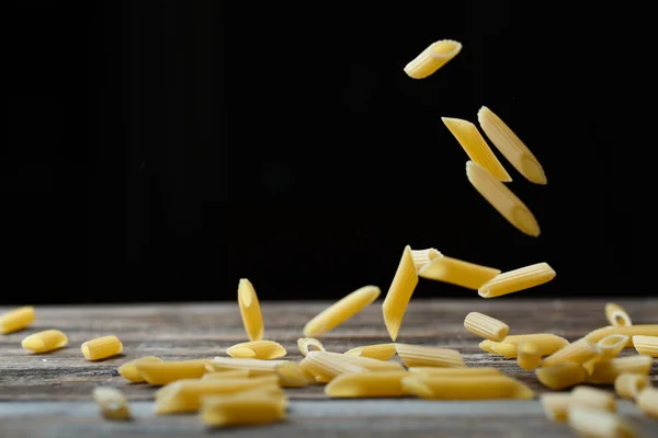 Caída de pasta de penne. Macarrones crudos amarillos voladores sobre fondo negro. — Foto de Stock