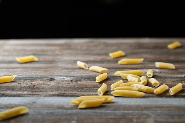 Massa de penne a cair. Voando macarrão cru amarelo sobre fundo preto. — Fotografia de Stock