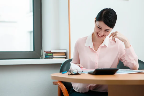 Молодая деловая женщина, сидящая на рабочем месте и читающая бумагу в офисе — стоковое фото