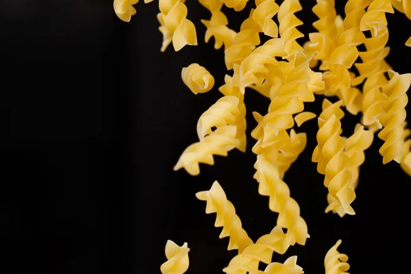 Pasta fusilli cadente. Maccheroni crudi gialli volanti su fondo nero . — Foto Stock