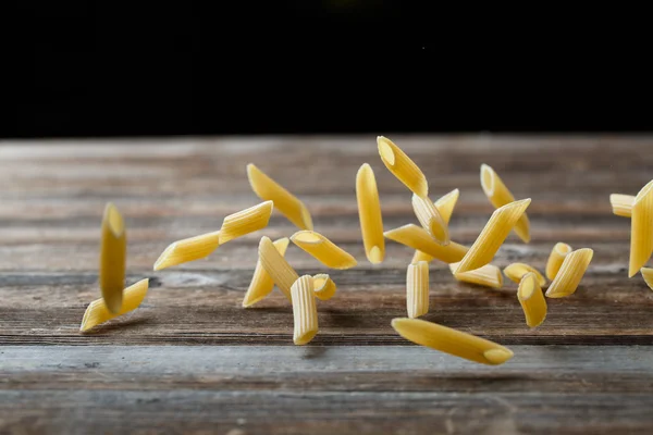 Spadający makaron penne. Latający żółty surowy makaron na czarnym tle. — Zdjęcie stockowe