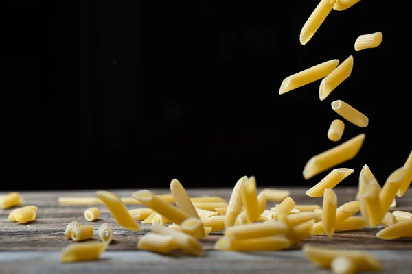 Massa de penne a cair. Voando macarrão cru amarelo sobre fundo preto. — Fotografia de Stock