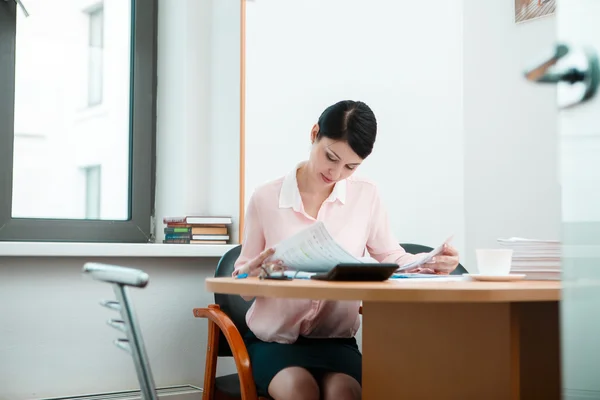 Junge Geschäftsfrau sitzt am Arbeitsplatz und liest Zeitung im Büro — Stockfoto